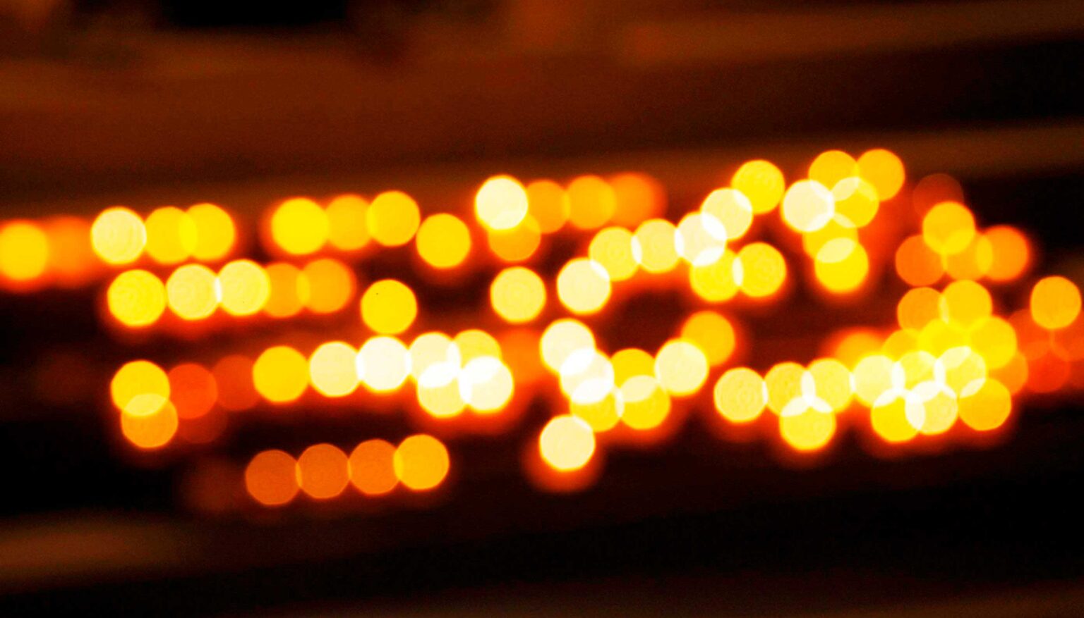 Unscharfe Aufnahme zahlreicher warm leuchtender Kerzenlichter in Gelb-, Orange- und Weißtönen vor dunklem Hintergrund.