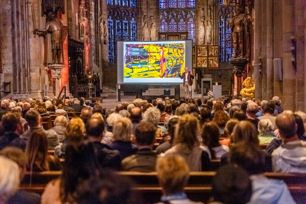 Zahlreiche Besuchnerinnen und Besucher verfolgen einen Vortrag mit großer Projektionsleinwand in der St. Reinoldi-Kirche.