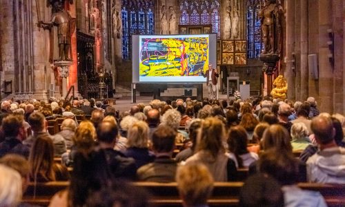 Zahlreiche Besuchnerinnen und Besucher verfolgen einen Vortrag mit großer Projektionsleinwand in der St. Reinoldi-Kirche.